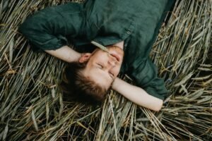 A man in a green shirt lying serenely on a field of wheat grass, exuding relaxation.