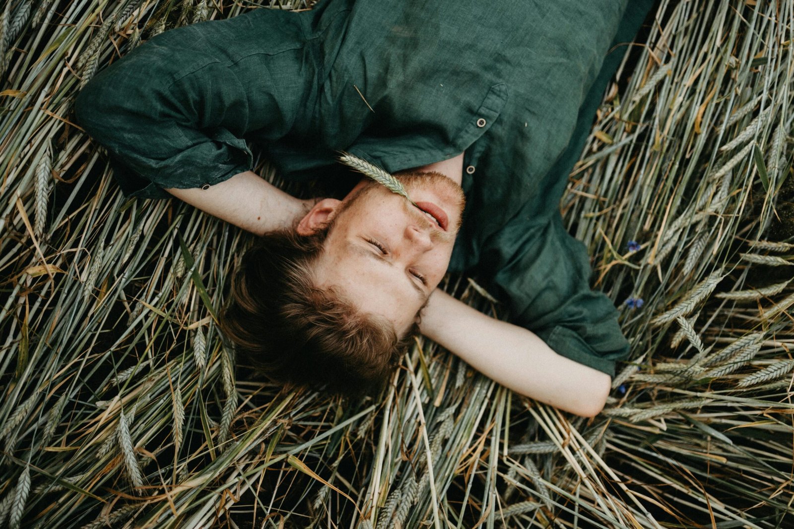 A man in a green shirt lying serenely on a field of wheat grass, exuding relaxation.