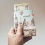Crop anonymous person showing banknotes with creative passport in hand on beige background